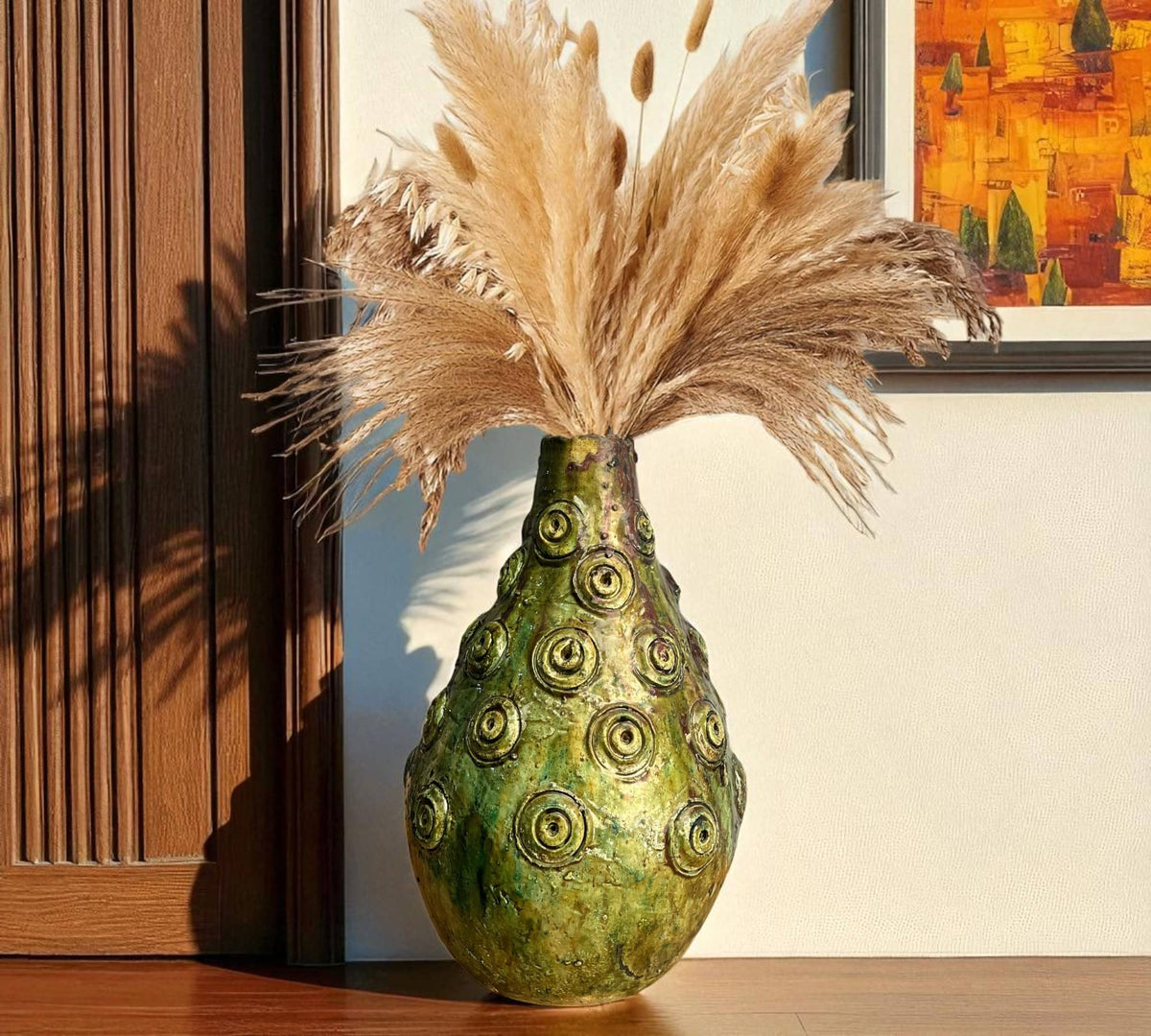 Decorative green vase with circular patterns and dried pampas grass on a wooden surface.