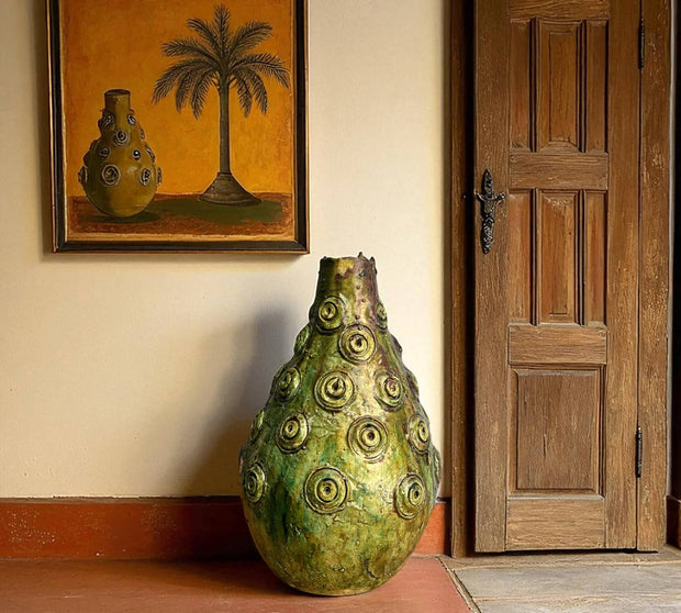 Decorative green vase with circular patterns in a room with a wooden door and wall art.
