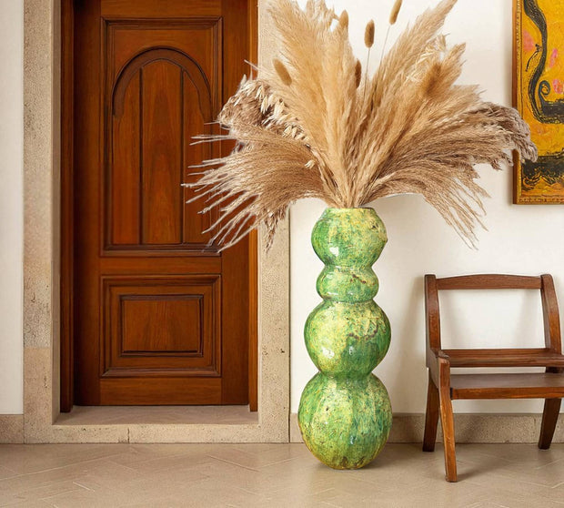 Decorative vase with dried pampas grass against a neutral wall with a wooden door and chair.