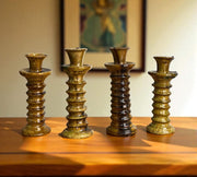 Four brown ceramic candle holders on a wooden surface with a blurred painting in the background.