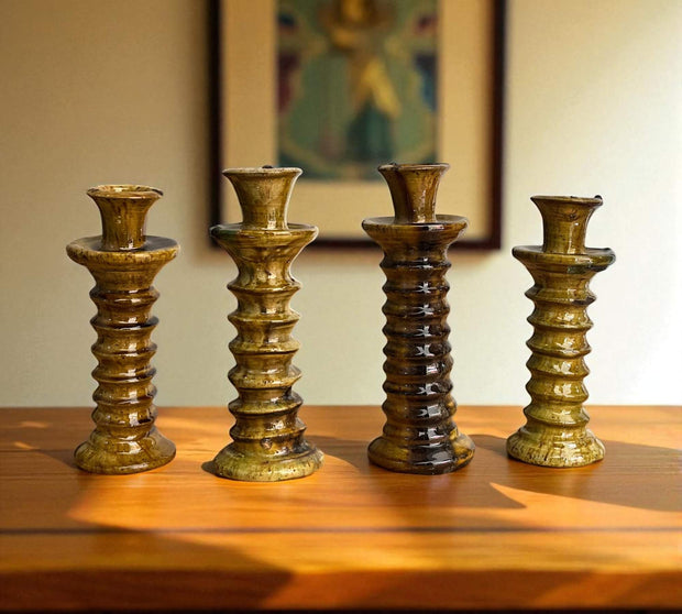 Four brown ceramic candle holders on a wooden surface with a blurred painting in the background.