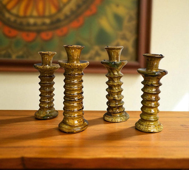 Set of four rustic candle holders on a wooden surface with a blurred painting in the background.