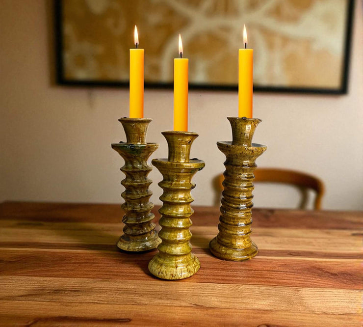 Three candle holders with lit candles on a wooden surface, framed artwork in the background.