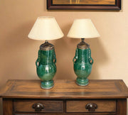 Two green ceramic lamps with white lampshades on a wooden table.