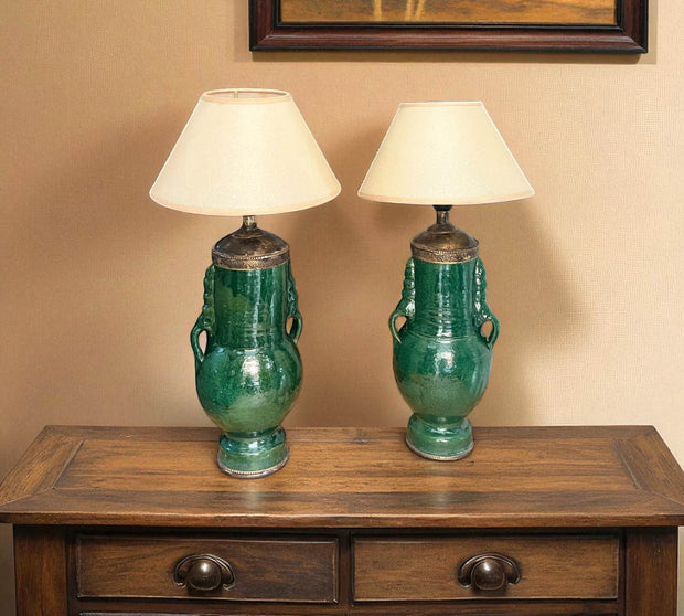 Two green ceramic lamps with white lampshades on a wooden table.