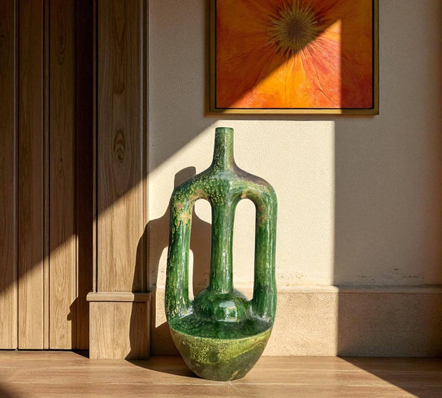 Green ceramic vase on a wooden surface with a wall painting in the background