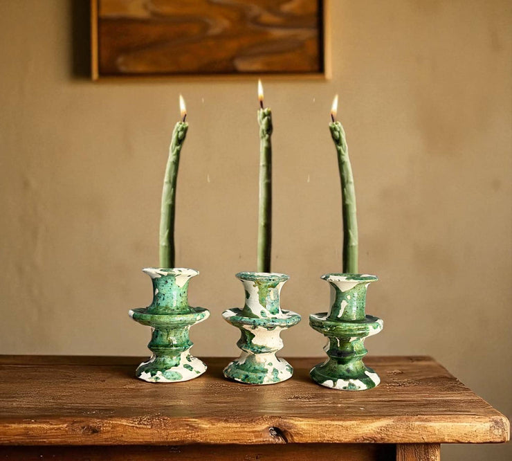 Three green ceramic candle holders with lit candles on a wooden surface against a beige wall.