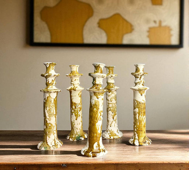 Set of five gold and white ceramic candle holders on a wooden surface with a neutral background.