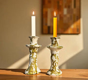 Two candlesticks with lit candles on a wooden surface against a neutral wall.