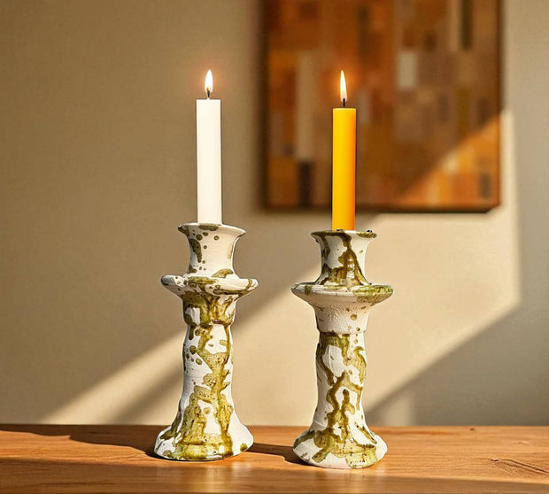 Two candlesticks with lit candles on a wooden surface against a neutral wall.