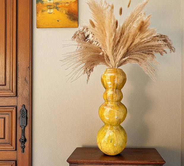 Yellow vase with dried pampas grass against a neutral wall.