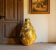 Decorative vase with gold and black patterns in a room with wooden door and wall art.