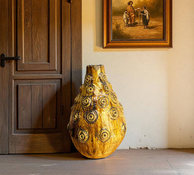 Decorative vase with gold and black patterns in a room with wooden door and wall art.