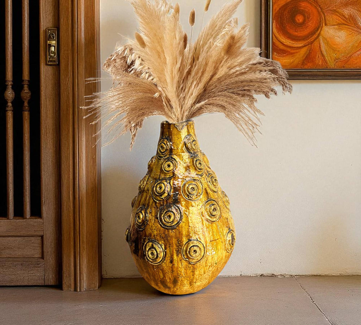 Decorative vase with ornate patterns and pampas grass against a neutral wall.