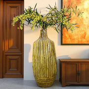 Yellow textured vase with flowers in a room with wooden door and cabinet.