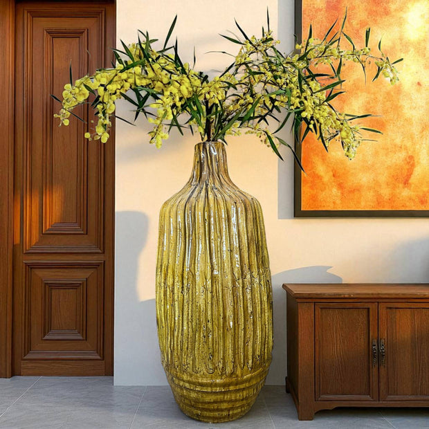 Yellow textured vase with flowers in a room with wooden door and cabinet.