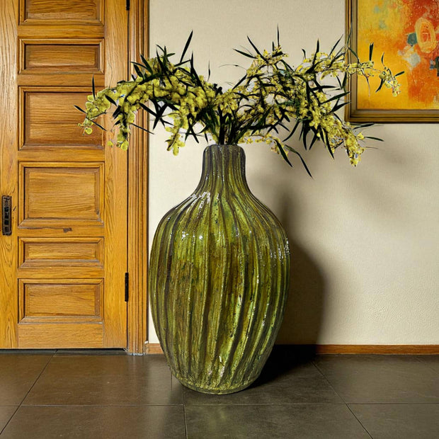Large yellow vase with flowers in a room with wooden door and wall art
