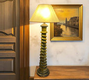 Decorative lamp on a wooden shelf with a painting of a canal scene in the background.