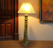 Floor lamp with a textured base in a room with wooden paneling and a painting on the wall.