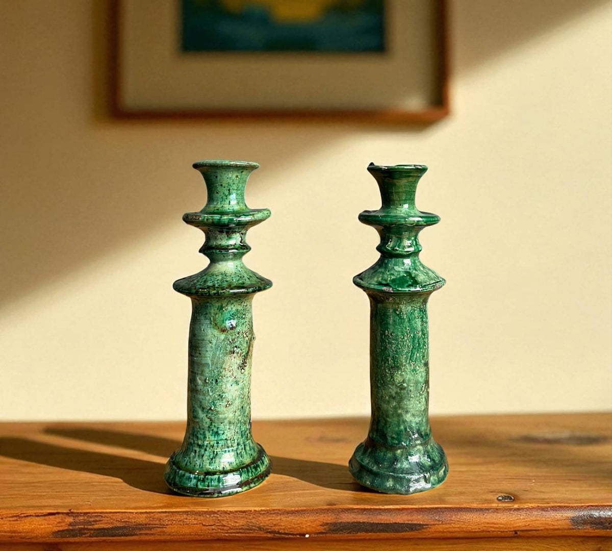 Two green ceramic candle holders on a wooden surface with a blurred background