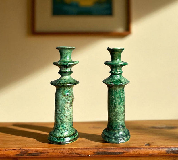 Two green ceramic candle holders on a wooden surface with a blurred background