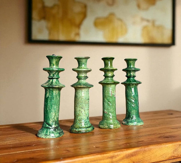Four green ceramic candle holders on a wooden surface with a blurred painting in the background.