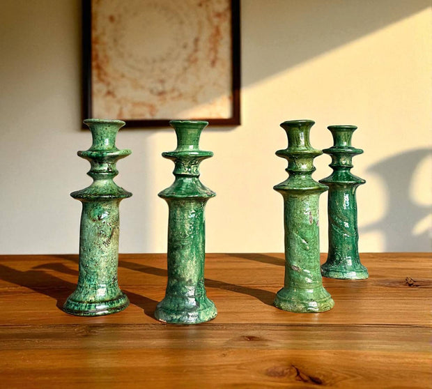 Set of four green ceramic candle holders on a wooden surface with a neutral background