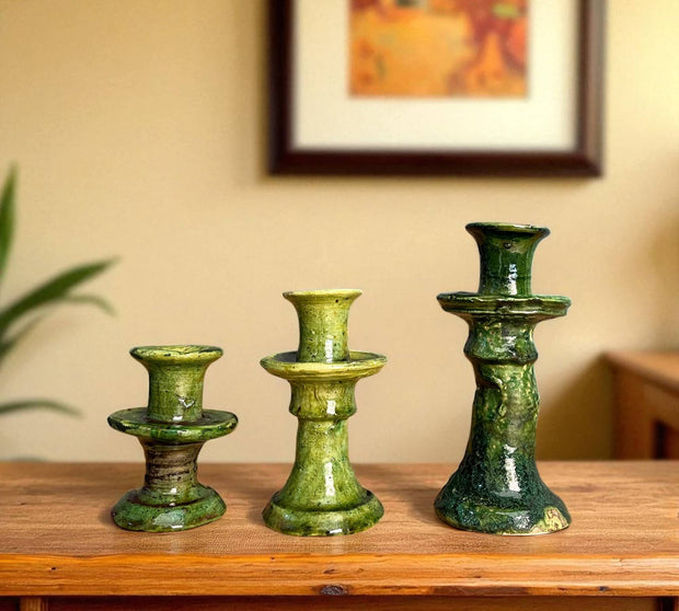 Three green ceramic candle holders on a wooden surface with a blurred background