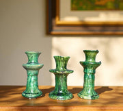 Three green ceramic candle holders on a wooden surface with a blurred background