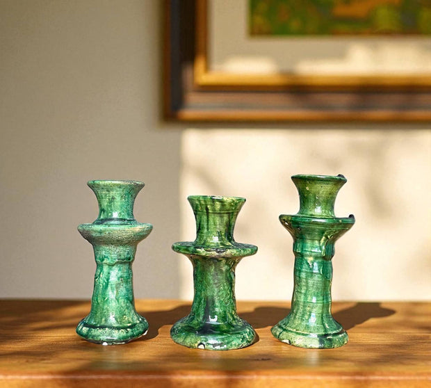 Three green ceramic candle holders on a wooden surface with a blurred background