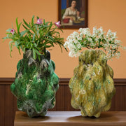 Two unique, textured vases with plants on a wooden surface against an orange wall.