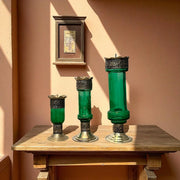 Vintage hand‑engraved silver‑plated brass and recycled glass candlesticks on a wooden table against a pink wall.