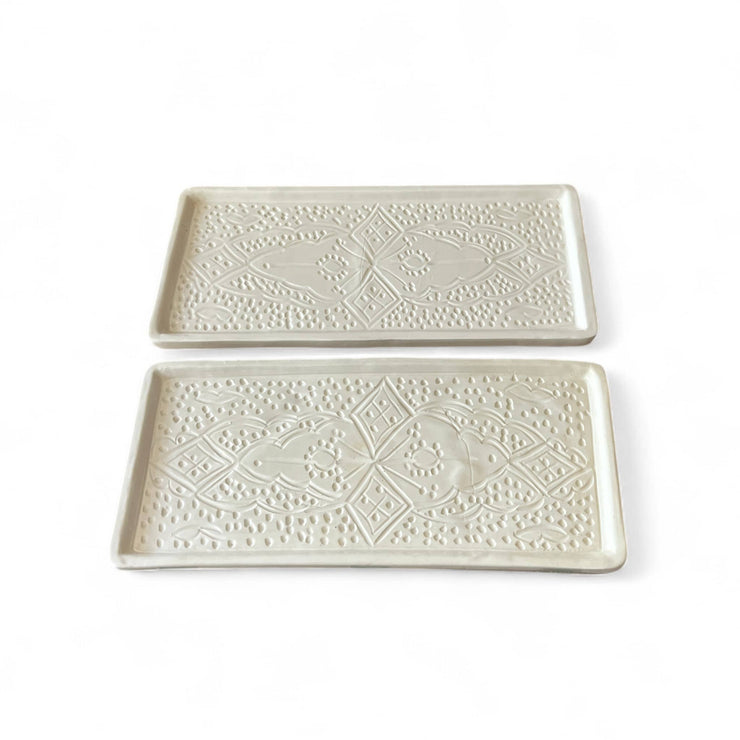 Two white ceramic trays with decorative patterns on a white background