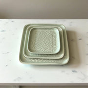 Two green ceramic trays with textured design on a marble surface