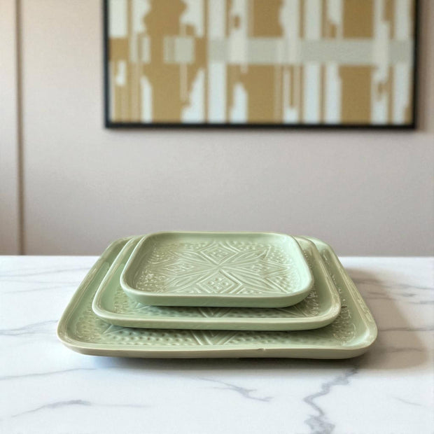 Set of green ceramic trays on a marble surface with abstract art in the background