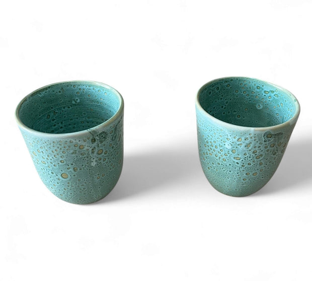 Two turquoise ceramic cups with a textured surface on a white background