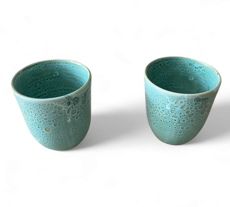 Two turquoise ceramic cups with a textured surface on a white background