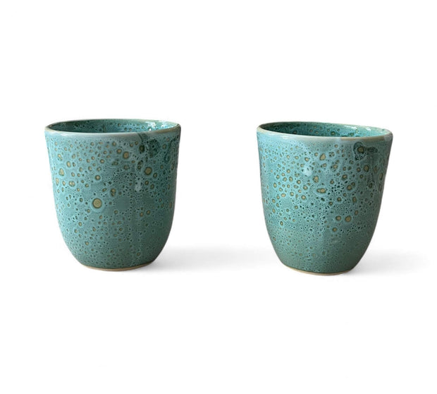 Two turquoise ceramic cups with a speckled texture on a white background